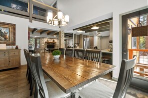 A spacious dining area with a wooden table and chairs, a chandelier, and a stone fireplace. - Evergreen (Big Bear Lake)