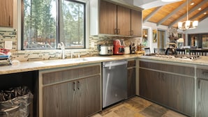 A modern kitchen with wooden cabinets, a stainless steel dishwasher, a coffee maker, and a gas stove. - Evergreen (Big Bear Lake)