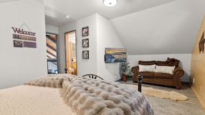 A bedroom with a large bed, a brown leather sofa, a wooden wall, and a painting on the wall. - Evergreen (Big Bear Lake)