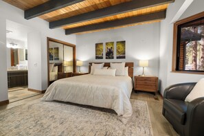 A bedroom with a large bed, wooden headboard, bedside tables with lamps, a mirror, and a window with blinds. - Evergreen (Big Bear Lake)