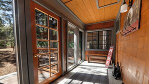 A wooden interior with a large glass door, a bench, and a welcome sign. - Evergreen (Big Bear Lake)