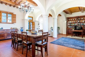 A spacious dining area with a wooden table and chairs, a chandelier, and a bookshelf filled with books. - GuestHost - Enchanting villa located within an agricultural estate on the Tuscan hills, surrounded by nature and with a breathtaking view of the surrounding countryside. The property, equipped with private outdoor parking, outdoor swimming pool, gym area (Palaia)