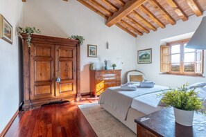 Ein Schlafzimmer mit einem Holzschrank, einem Bett mit weißer Bettdecke, einer Kommode und einem Fenster mit Ausblick.