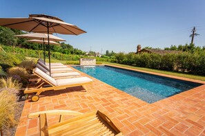 Ein Pool mit Liegestühlen und Sonnenschirmen, umgeben von viel Grün und einer Pflasterterrasse.