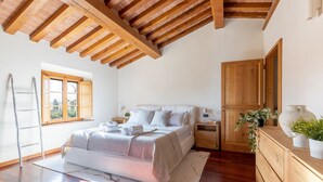 Ein Schlafzimmer mit Holzboden, einem Bett mit weißer Bettwäsche, einem Nachttisch, einer Kommode und einem Fenster mit Aussicht.