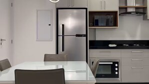 A modern kitchen with a refrigerator, microwave, oven, and a dining table with chairs. - Ocean View, New Apartment with Garage and BBQ (Itapema)