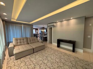 A modern living room with a sectional sofa, a patterned rug, recessed ceiling lighting, and a flat-screen TV. - 4 Suites • Private Playground • Grill (Itapema)