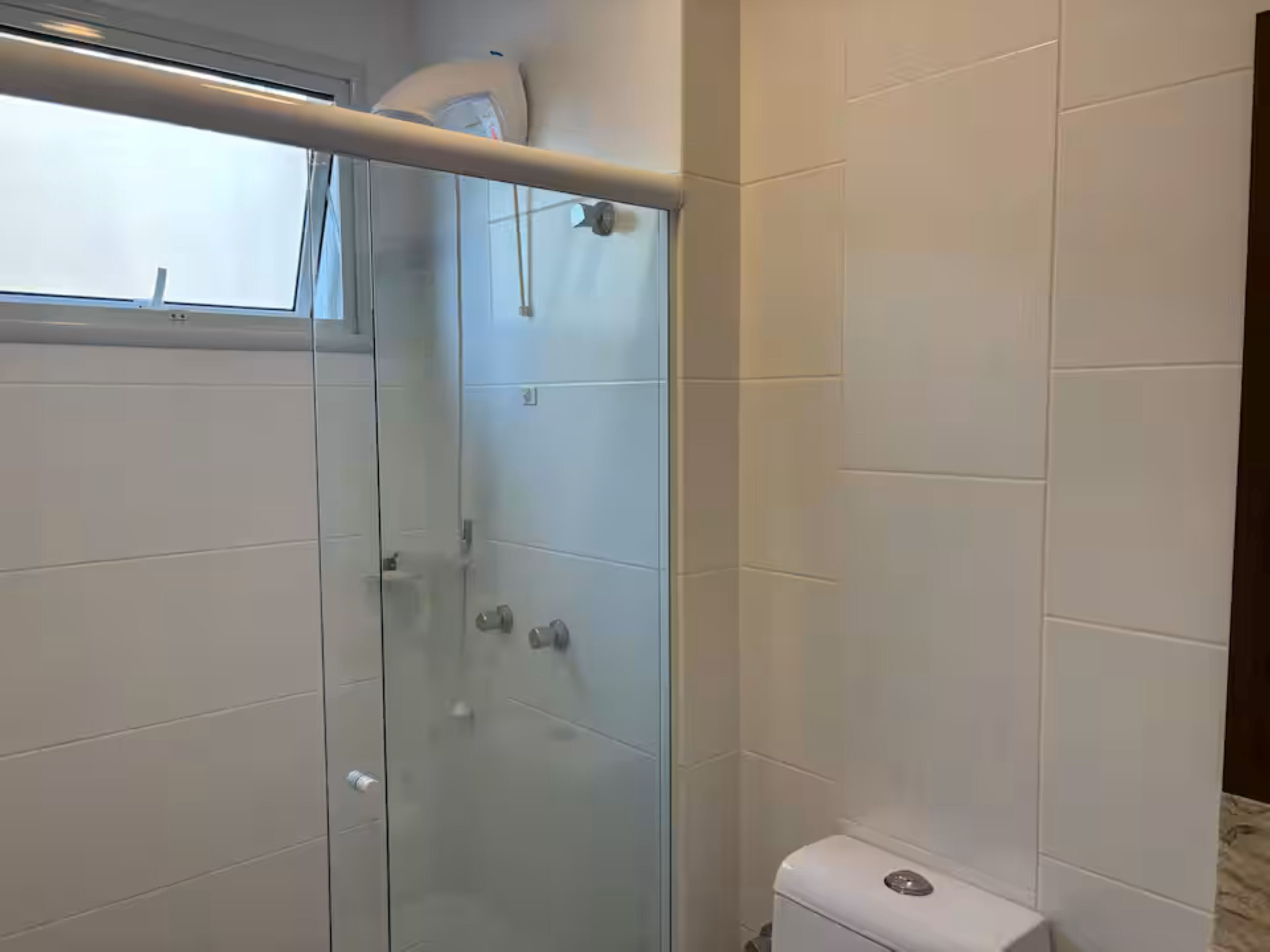 Kylpyhuone, jossa on valkoiset laatat, lasinen suihkuseinä ja wc.