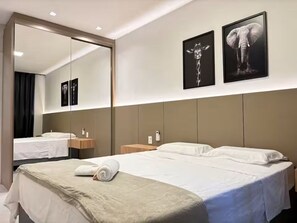 A hotel room with a large mirror, two beds, a bedside table, and artwork on the wall. - 3 Suites, Perequê Beach with BBQ (Porto Belo)