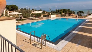 Una piscina con tumbonas y sombrillas, rodeada de árboles y vistas al mar.