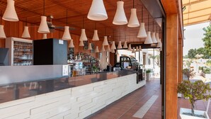Zona de bar con mostrador, lámparas colgantes y un refrigerador a la vista lleno de vasos.