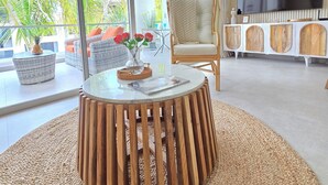 Un soggiorno moderno con una grande televisione, un tavolino rotondo in legno, mobili in vimini e vista su palme.