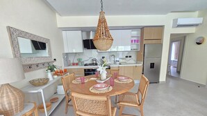 Una cucina moderna con mobili bianchi, un'area pranzo con sedie in vimini e un tavolo rotondo, e un lampadario.