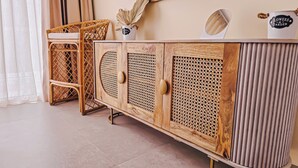 Un armadietto in legno con decorazioni intrecciate, una sedia in vimini e uno specchio appeso al muro.