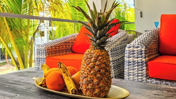Una camera a tema tropicale con un balcone, un'ananas e un piatto di frutta su un tavolo.