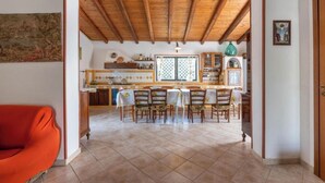A dining area with a wooden ceiling, tiled floor, and a kitchen in the background. - Peaceful Countryside Villa - 8 Mins to Guidaloca Beach & Scopello (Sicilia)