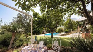 A patio with a table set for two, a hammock, and a pool in the background. - Peaceful Countryside Villa - 8 Mins to Guidaloca Beach & Scopello (Sicilia)
