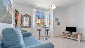 Una sala de estar con sofá, televisor, aparador y ventana con cortinas.
