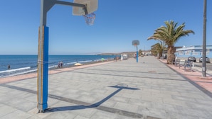 Una cancha de baloncesto con una red, una palmera y una playa al fondo.