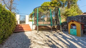 Une aire de jeux avec des balançoires, une petite maison de jeu et un mur en pierre.
