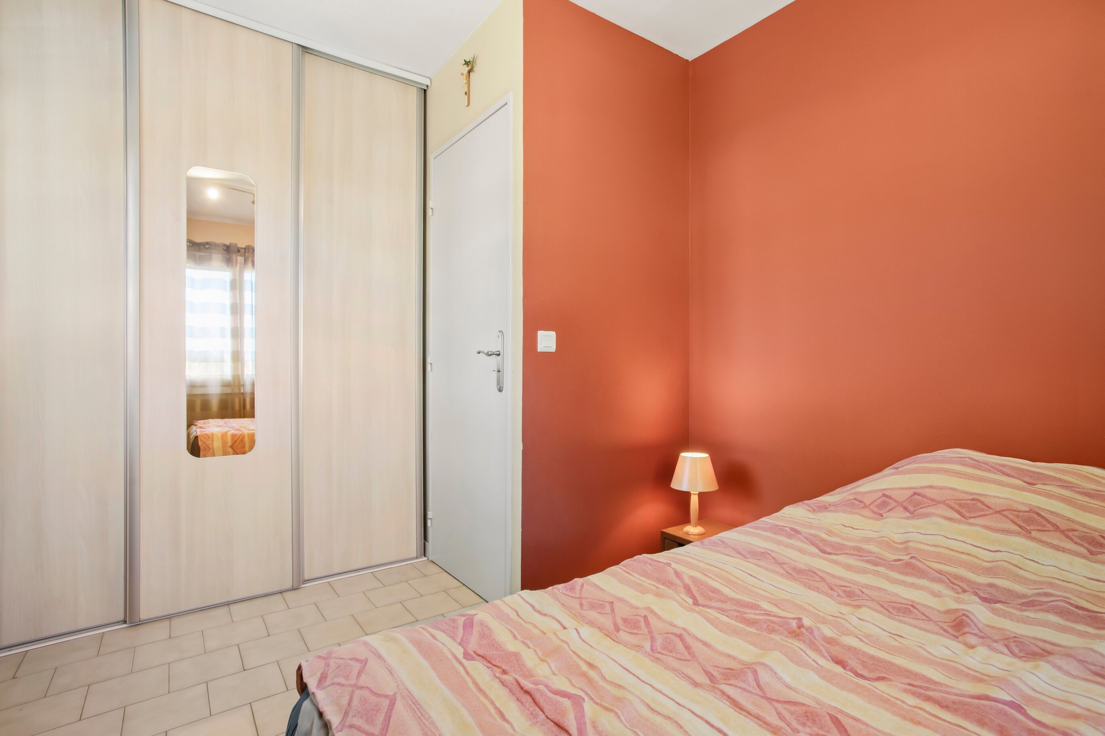 Une chambre à coucher comprenant un lit, une armoire, une table de chevet avec une lampe et un miroir.