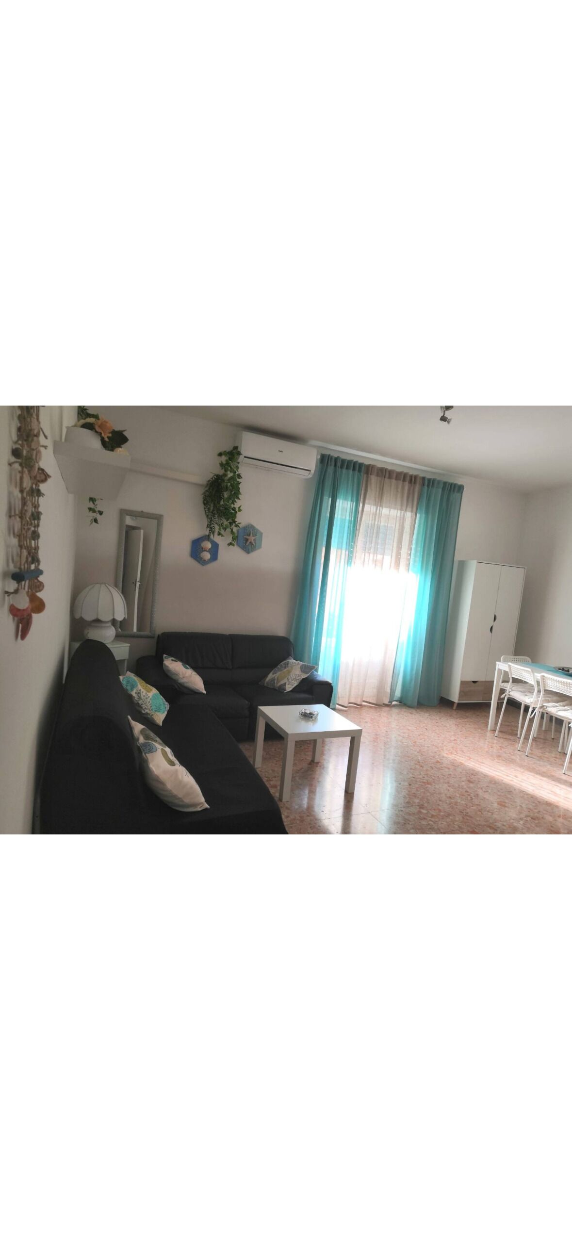 En stue med en sort sofa, et lille bord, et hvidt skab og et vindue med gardiner.