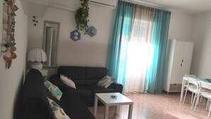 Un saló amb un sofà negre, una taula petita, un moble blanc i una finestra amb cortines.
