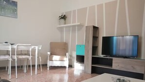 Un saló amb un sofà blanc, una taula blanca, una televisió i un quadre a la paret.