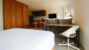 Hotellihuone, jossa on sänky, työpöytä tuolilla, pieni keittiönurkkaus ja televisio.