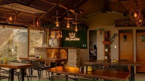 Ein Restaurant mit Holztischen und -stühlen, hängenden Lampen und einer grünen Wand mit einem Logo.