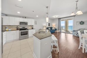 A modern kitchen with white cabinets, a central island, and a dining area with a blue sofa and white chairs. - Gulf View, King Bed, Pools, Tiki Bar Small dogs ok (Panama City Beach)