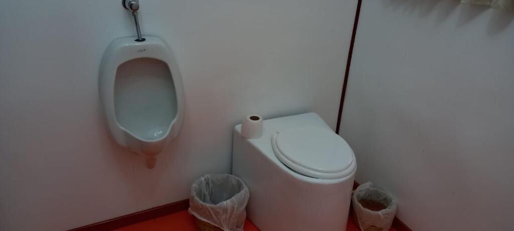 A restroom with a urinal, toilet, and two trash bins.