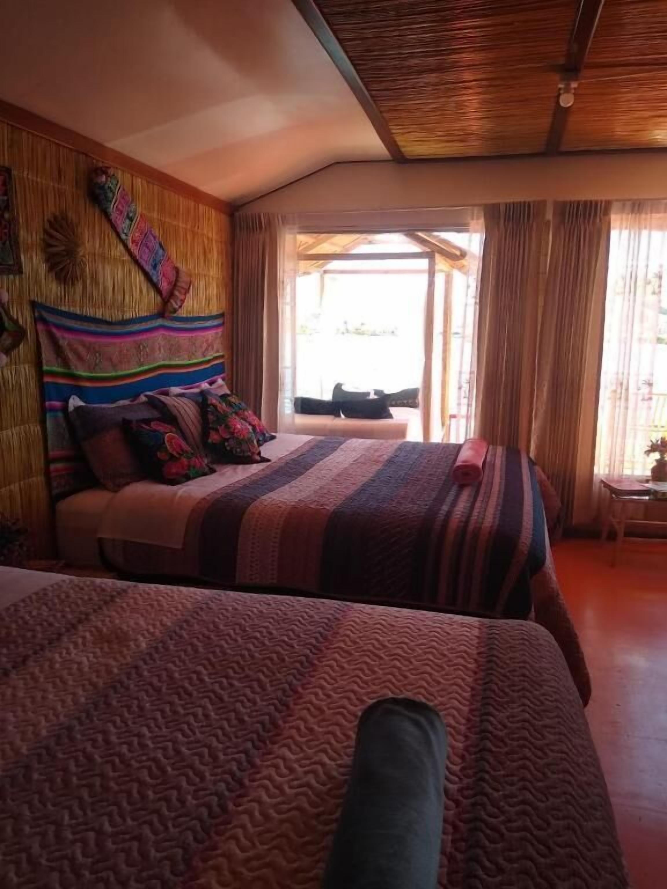 Een kamer met twee bedden, een houten plafond en uitzicht door een raam.