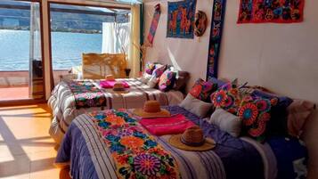 A room with two beds, colorful blankets, and a view of the water.