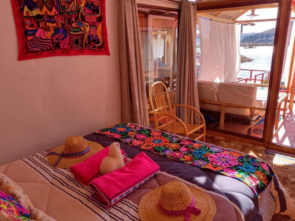 A room with a bed, a colorful woven blanket, a straw hat, and a view of the sea through a glass door.