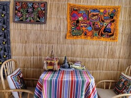 Una habitación con un muro tejido, un mantel colorido a rayas y dos sillas.