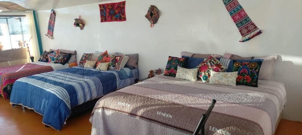 A room with two beds, each with multiple pillows and blankets, a wooden floor, and a window.