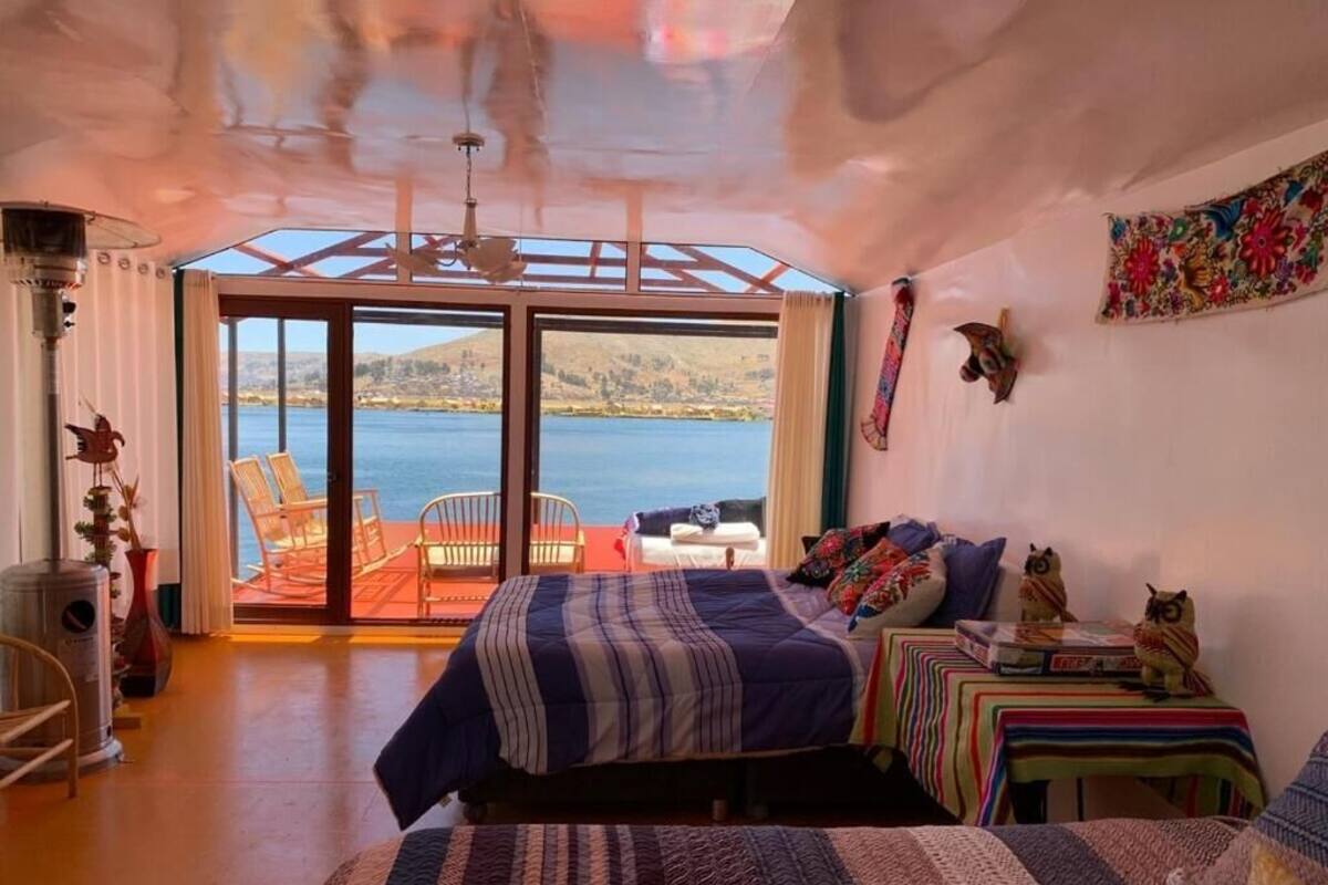 Un dormitorio con una cama grande, una mesita pequeña, dos sillas y vista a un cuerpo de agua.