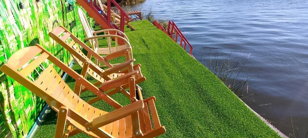 A row of wooden lounge chairs by a body of water with a red railing.