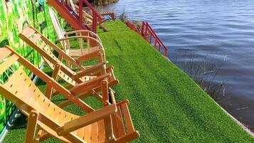 A row of wooden lounge chairs by a body of water with a red railing.