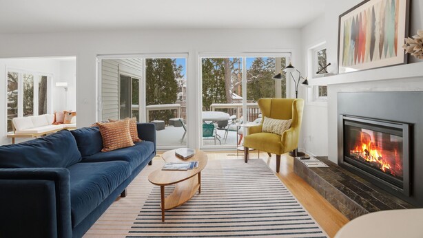 A living room with a blue sofa, a yellow armchair, a fireplace, and a view through large glass doors. - Lake of the Isles Retreat (Minneapolis)