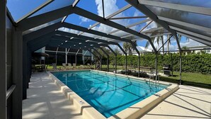 Piscina com teto de vidro, rodeada por espreguiçadeiras e um gramado bem cuidado.