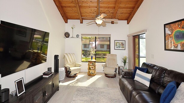 Uma sala de estar com ventilador de teto, uma televisão grande, um sofá de couro e um espaço de jantar com mesa e cadeiras.