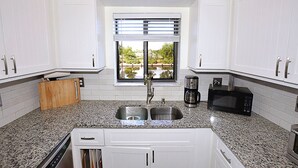 Cozinha com armários brancos, bancada de granito, pia dupla, cafeteira e micro-ondas.