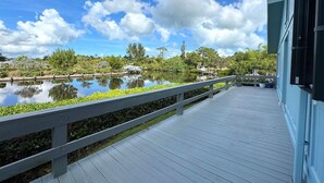 Um deck de madeira com guarda-corpo, com vista para águas calmas, cercado por vegetação e um céu claro.