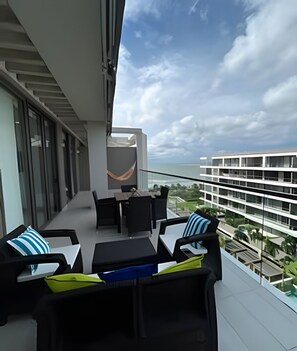 Ein Balkon mit Sitzgelegenheit im Freien, einer Hängematte und Blick auf ein modernes Gebäude sowie das Meer.