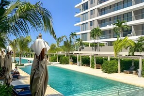 Ein modernes Hotel mit Schwimmbad, Palmen und blauem Himmel.