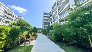 Een modern gebouw met meerdere verdiepingen, een pad met bankjes en weelderige begroeiing.