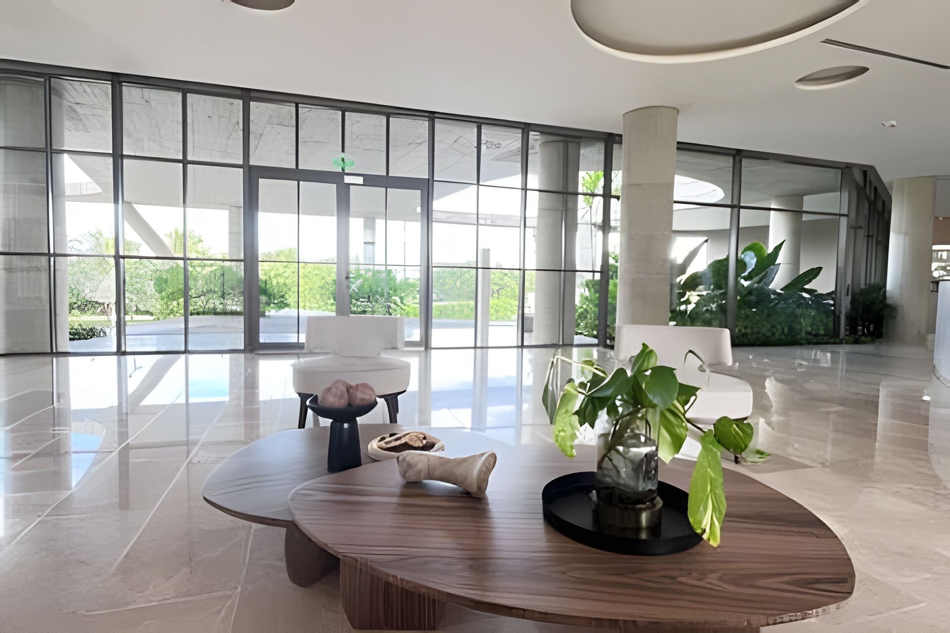 A spacious lobby with a large glass wall, a round wooden table, and a potted plant.