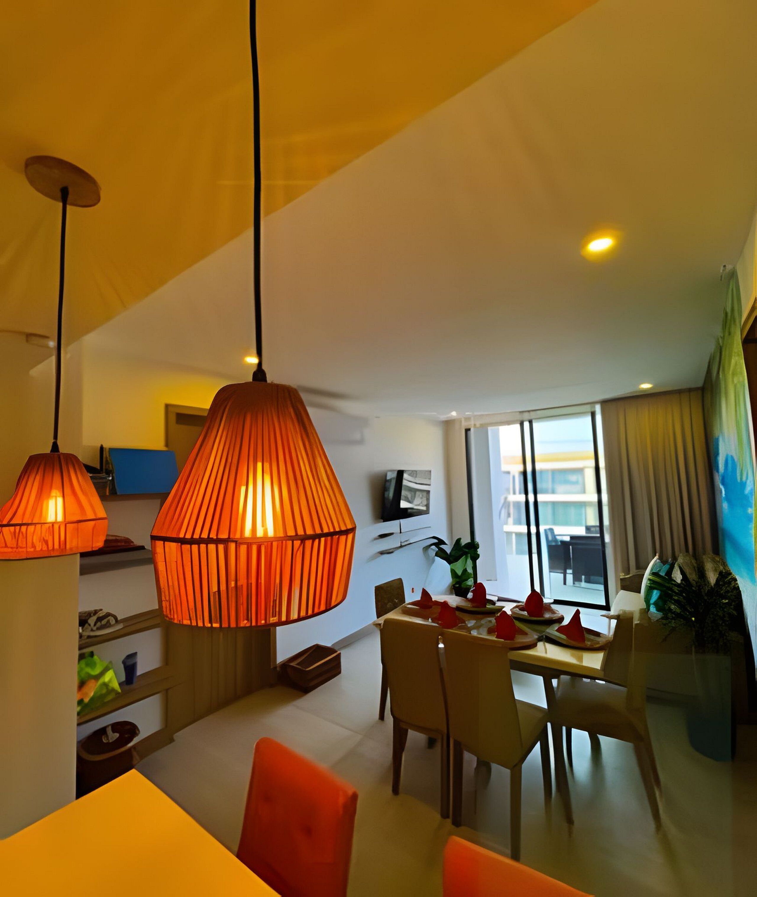 A dining area with a table set for four, overhead pendant lighting, and a view of a balcony through a large window.